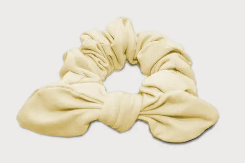 The Goodnighties Knotted Bow Scrunchie in beige, made from thermoregulating fabric in the USA, is displayed on a white background. This stylish hair accessory adds charm and comfort to any look.