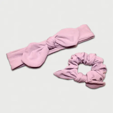 The Goodnighties Matching Knotted Bow Headband & Scrunchie set features a pink headband with a large bow beside a matching scrunchie, creating an adorable hair accessory duo on a light gray background.