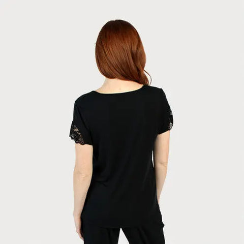 A person with long red hair stands with their back to the camera, wearing the Goodnighties Lace Accent Scoop Neck Tee featuring intricate sleeve details, set against a plain light gray background.