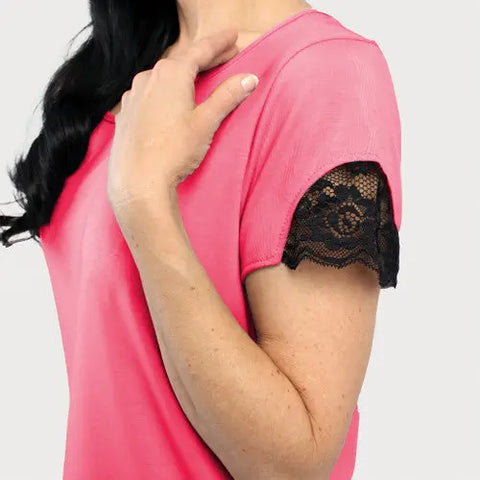 A person wearing the Goodnighties Lace Accent Scoop Neck Tee, featuring pink fabric and black lace-trimmed sleeves, touches their collarbone against a plain light background.
