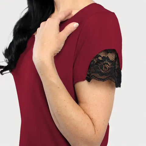 A person is shown from the shoulders up, wearing the Goodnighties Lace Accent Scoop Neck Tee in maroon with black lace-trimmed short sleeves, and resting one hand on their opposite shoulder.