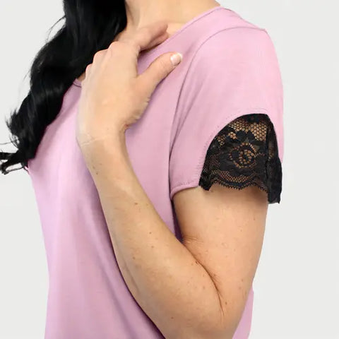 A person wears the Goodnighties Lace Accent Scoop Neck Tee in light pink with short sleeves and black lace trim—ideal as American-made sleepwear or stylish loungewear.