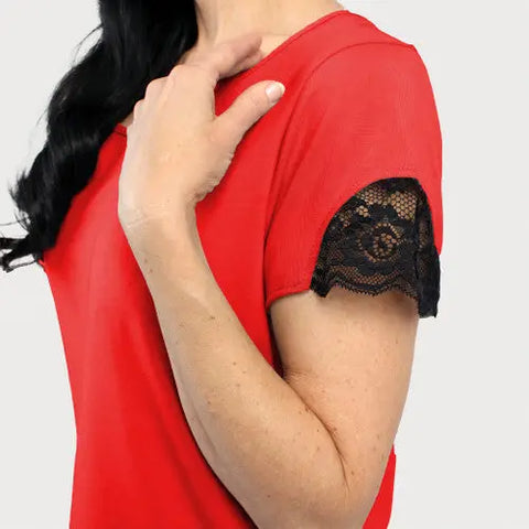 A person in a Goodnighties Lace Accent Scoop Neck Tee with red fabric and black sleeve trim is touching their shoulder; only the upper body is shown.