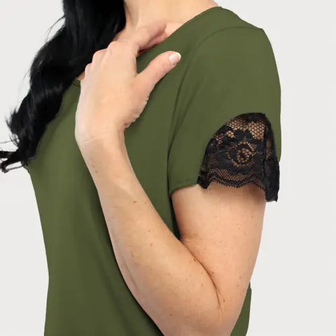 A woman models the Goodnighties Lace Accent Scoop Neck Tee in olive green with black trim, her hand on her shoulder against a light backdrop—an ideal choice for chic, moisture-wicking loungewear.