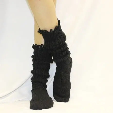 A person wears Catherine Cole LACE Topped Ultimate Slouch Socks in black, featuring ruffled lace trim. Only the lower legs and feet are shown against a white background, highlighting these stylish womens accessories.