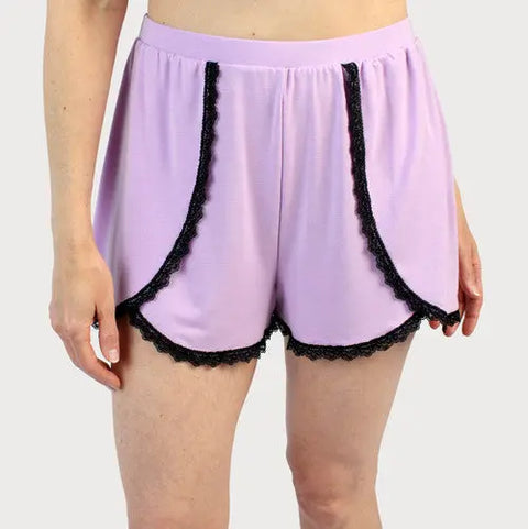 A person wears Goodnighties Lace Trim Tulip Shorts in light purple with black lace edges, featuring a high waistband and loose, comfortable fit. The American-made sleepwear is styled against a plain light background.