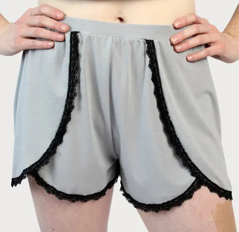A person in Goodnighties Lace Trim Tulip Shorts stands with hands on hips against a plain background, showcasing comfortable, American-made sleepwear ideal for relaxation.