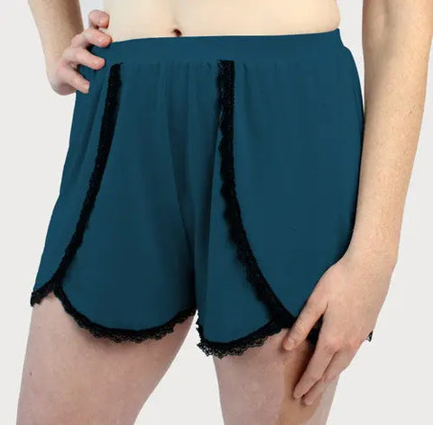 Model wears Goodnighties Lace Trim Tulip Shorts in teal, featuring overlapping front panels and a scalloped hem. These moisture-wicking loungewear shorts are perfect for relaxing, shown against a plain light background with one hand on hip.
