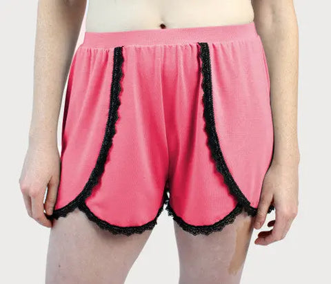 A person models the high-waisted, pink Goodnighties Lace Trim Tulip Shorts with black lace edging against a plain light background.
