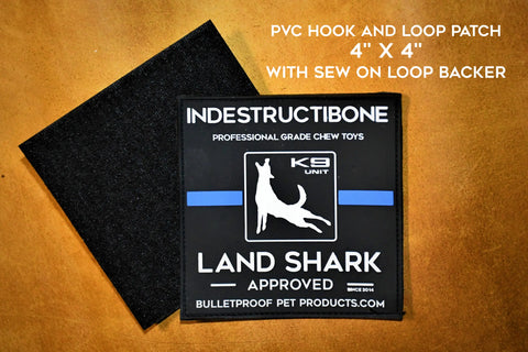 A 4x4 black LAND SHARK HOOK and LOOP PVC PATCH - Thin Blue Line by Bulletproof Pet Products Inc, featuring a dog silhouette and “Indestructibone Land Shark Approved,” shown with its sew-on loop backer on a brown background.