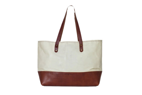 The Urban Southern Large Canvas Tote features full-grain leather accents on the handles and bottom with a cream-colored canvas upper, shown against a white background.