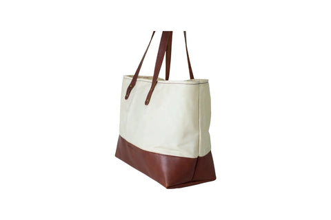 The Urban Southern Large Canvas Tote, featuring full-grain leather accents on the bottom and handles, is photographed against a white background at an angle to show both the front and one side. Made in America.