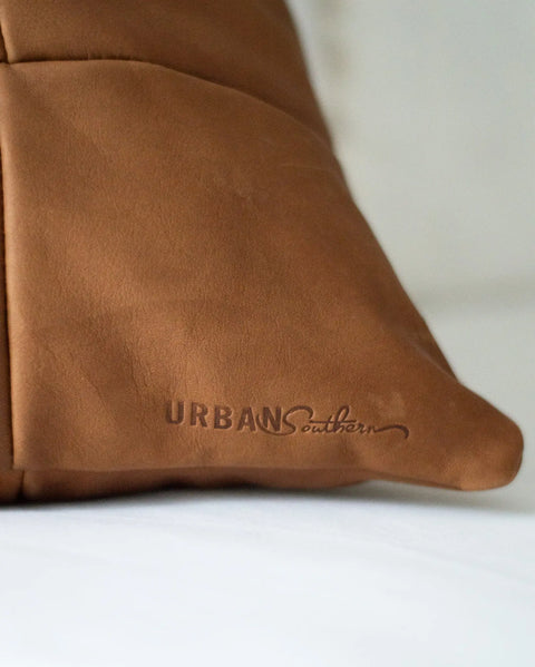 Close-up of the Large Leather Pillow by Urban Southern, featuring rich brown leather with the brand’s name embossed on the surface, shown against a white background.