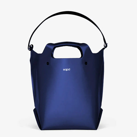 The LastBag - Shoulder by eqpd is a modern dark blue tote with sturdy handles, a black adjustable strap, and a small white logo on the front—designed for everyday durability, shown against a plain white background.