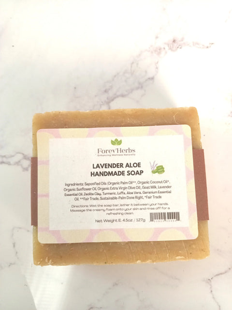 A 4.5 oz (127g) bar of Forev'Herbs Lavender Aloe Handmade Soap rests on a white surface. Its label features natural ingredients ideal for sensitive skin.