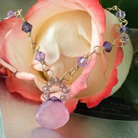 The Purple Chalcedony Drop 14 KT Gold Filled Gemstone Collier Necklace by Alexa Martha Designs features a large faceted pink pendant accented with purple and pink beads, elegantly displayed on a pale blush rose with peach edges.