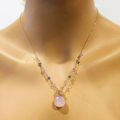 The Alexa Martha Designs Purple Chalcedony Drop 14 KT Gold Filled Gemstone Collier Necklace features pink, purple, and clear beads with a large teardrop-shaped pink pendant, elegantly displayed on a mannequin bust.