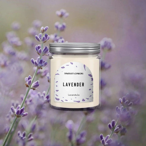 Amid blooming lavender, the Sawdust & Embers Lavender - Signature Candle in a glass jar with a silver lid radiates calming fragrance, offering a handcrafted, premium soy candle experience.