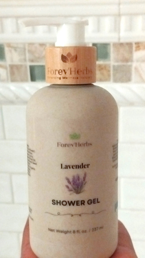 A hand holds a Forev'Herbs Lavender Shower Gel bottle with a wooden pump top, in front of a tiled bathroom wall. The label highlights lavender essential oil, an illustrated sprig, and shows 8 fl. oz. (237 ml).