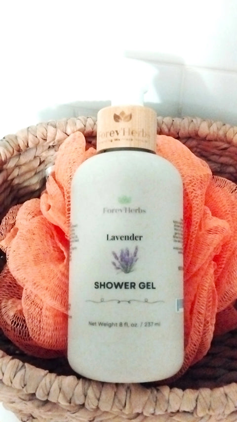 A bottle of Forev'Herbs Lavender Shower Gel rests in a woven basket with an orange bath pouf, set against a white tiled background.