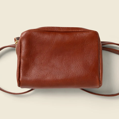 The CASUPO Leather Fanny Pack in Chocolate is a small, handcrafted square-shaped brown leather bag with a simple design and thin strap, shown against a light beige background.
