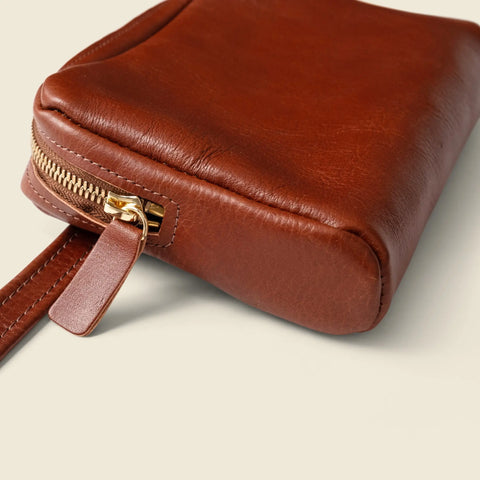 A close-up of the CASUPO Leather Fanny Pack - Chocolate shows its gold zipper and leather pull tab, displayed on a light-colored surface.