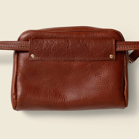 The CASUPO Leather Fanny Pack - Chocolate features a handcrafted brown leather design with a front flap, two brass studs, and a textured surface, shown against a plain light background.