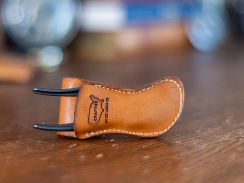 A veg-tanned cowhide Leather Tool Holster for Knipex 4 XS Pliers by KC Laser Co, with white stitching and logo stamp, holds a black metal tool and rests on wood. USA made belt pouch case.