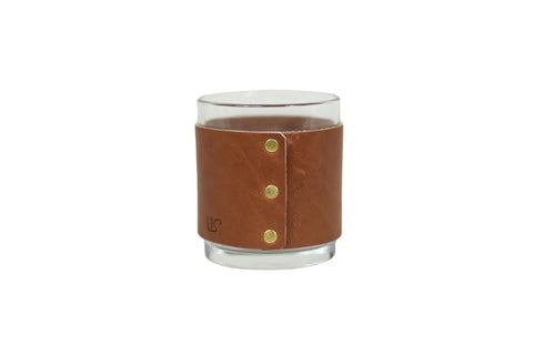 The Urban Southern Leather Wrapped Whiskey Glass features a clear tumbler wrapped in brown full-grain leather, secured with three brass rivets and an embossed logo—an elegant upgrade for any bar cart.