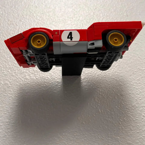 A Lego Speed Champion racecar is displayed upside down on a textured white wall using the Chatelet Manufacturing Collectible Wall Display, a USA-made side car display mount compatible with Lego Speed Champion racecars.