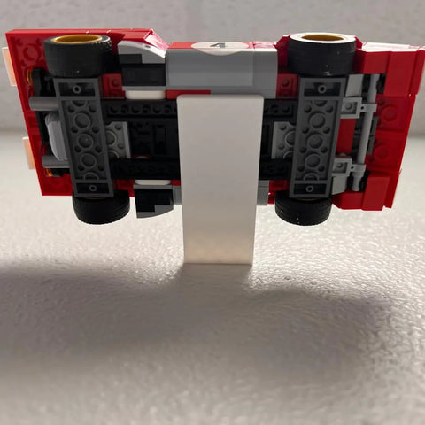 A red Lego Speed Champion Racecar is displayed upside down on the Chatelet Manufacturing Collectible Wall Display, compatible with Lego Speed Champion racecars—perfect as a side car display wall mount. Made in USA (Side Profile).