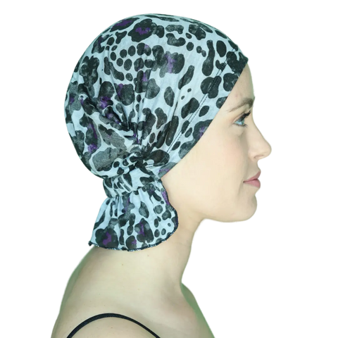 A woman in profile wears the Chemo Beanies® Katy, a black and purple leopard print chemo head cover, with a clear background emphasizing her face and the stylish Scarves - Chemo Beanies® slip-on beanie by Chemo Beanies®.