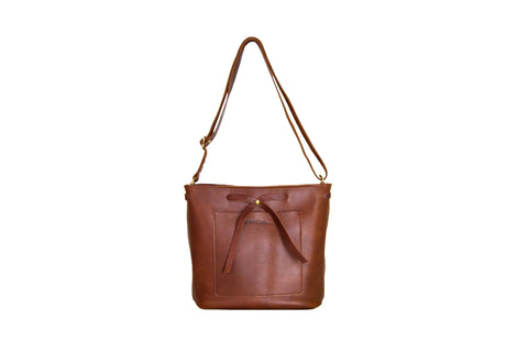 The Lexington Bow by Urban Southern is a brown leather crossbody shoulder bag with a front pocket, decorative leather bow, and adjustable strap, shown against a white background.
