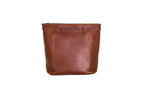 The Lexington Bow by Urban Southern is a brown leather tote with a rectangular front pocket and cutout handle, stylishly displayed against a white background.