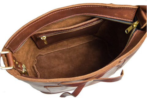 Open top view of an empty Lexington Bow crossbody by Urban Southern in brown leather reveals a suede interior, inner zippered pocket, and brass hardware—an elegant accessory for any occasion.