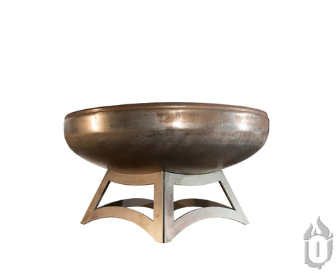 The Ohio Flame Liberty Fire Pit With Hollow Base, made in the USA, features a large, round weathered steel bowl with a copper-like finish set on a sturdy, modern metal base against a white background.