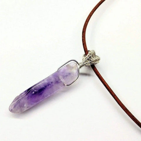 The Silver Wrapped Light Amethyst Gemstone Point Leather Necklace by Alexa Martha Designs features a light amethyst point wrapped in sterling silver, hanging from a brown leather cord and displayed against a white background.