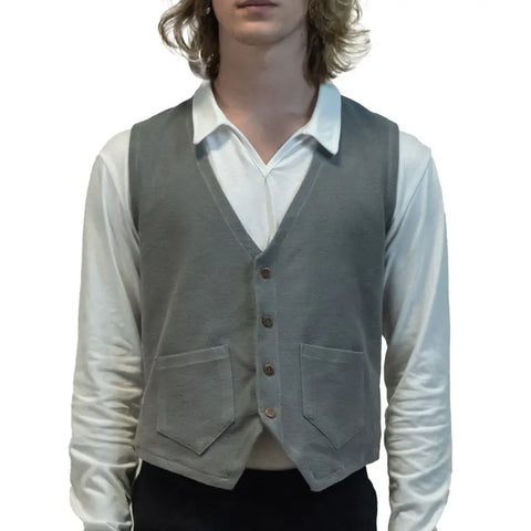 A person with shoulder-length wavy hair wears the Spiritex | Sustainable Apparel Vanderbilt Vest in light gray with two front pockets over a white collared shirt, shown from the waist up against a plain white background.