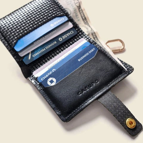 The CASUPO Wallet With Snap and Key Ring - Black Limited Edition is open, displaying Chase cards, a folded U.S. dollar bill, and a small key inside. The wallet rests on a light surface.