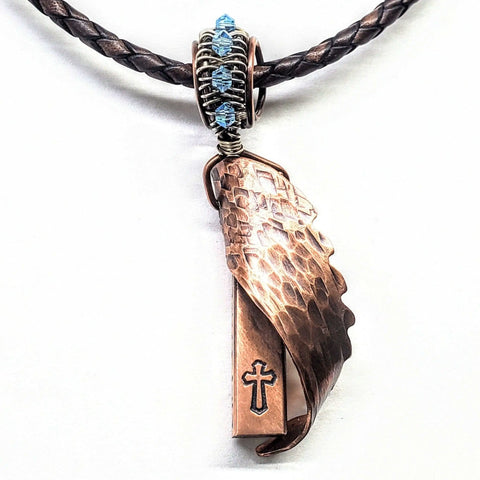 Close-up of the Memorial Birthstone Angelwing Necklace–Limited Special Edition 2020-2024 by Alexa Martha Designs, featuring a custom copper rod with angel wing and cross, plus blue wire and bead accents on a braided leather cord.