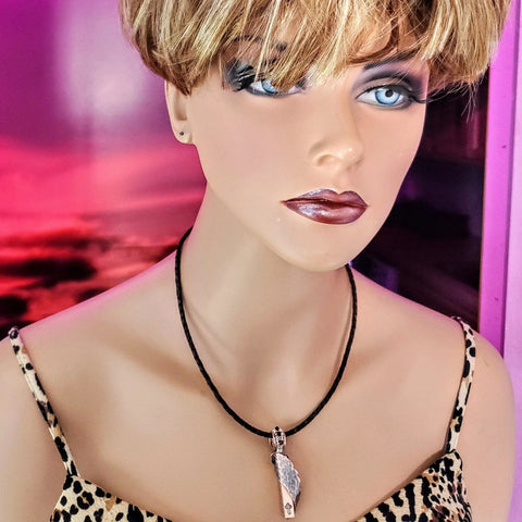 A mannequin with short blonde hair, blue eyes, and dark makeup models a leopard print top and Alexa Martha Designs’ Memorial Birthstone Angelwing Necklace—Limited Special Edition 2020-2024—set against a pink and purple background.