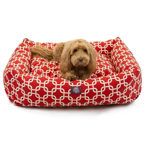 A small, fluffy brown dog relaxes on a Majestic Pet Links Luxe Bagel Bed - Personalized, featuring a red and white geometric washable slipcover, plush fiberfill, and raised sides for extra comfort.