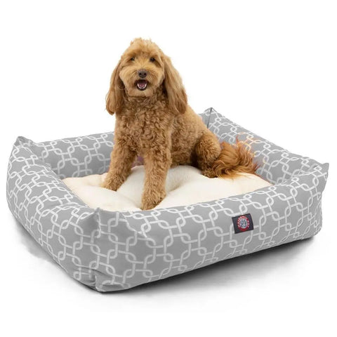 A small, curly-haired brown dog lounges comfortably on a Majestic Pet Links Luxe Bagel Bed - Personalized, featuring a washable slipcover, plush fiberfill, gray and white pattern, raised sides, and a soft cushion.