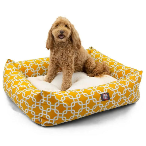 A small, curly-haired brown dog sits happily on a Majestic Pet Links Luxe Bagel Bed - Personalized, featuring plush fiberfill, raised sides, and a washable yellow and white slipcover with a soft cream cushion.
