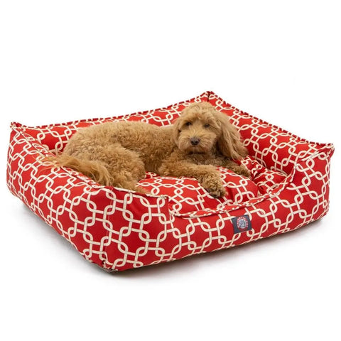 A fluffy light brown dog relaxes on the Majestic Pet Links Contemporary Lounge Bed, featuring premium fiberfill and a red rectangular slipcover with a white geometric pattern.