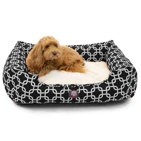 A small, fluffy tan dog relaxes on a soft cream cushion inside the Majestic Pet Links Contemporary Lounge Bed, a rectangular black bed featuring a white geometric pattern and premium fiberfill for added comfort.