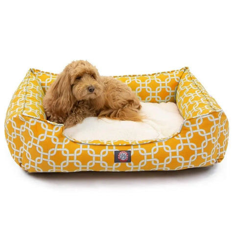 A fluffy light brown dog is lying on a soft, cream-colored cushion inside the Majestic Pet Links Contemporary Lounge Bed, a yellow luxurious bed with a white geometric pattern and a machine washable slipcover.
