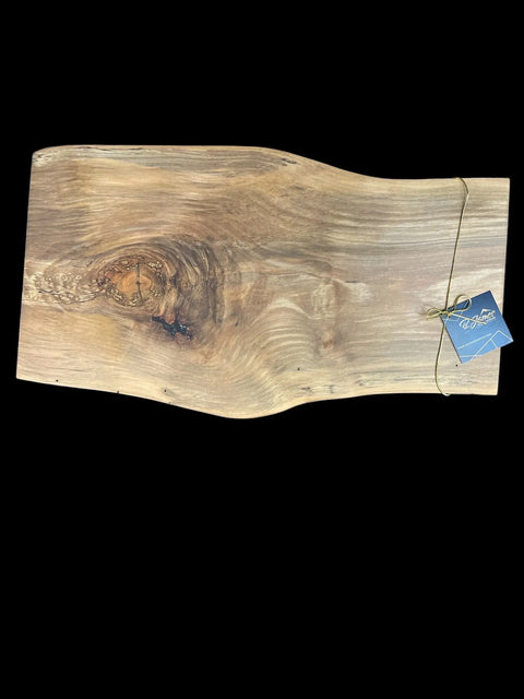 The B. James Design & Woodwork Live Edge Ambrosia Maple Serving Tray features natural grain patterns, a knot, distinctive uneven edges, and is accented with a gold string and blue tag in the top right corner against a black backdrop.