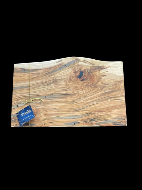 The Ambrosia Live Edge Serving Tray by B. James Design & Woodwork features a natural wood finish with a wavy grain and central knot, tied with a yellow string and blue tag, displayed on a black background.