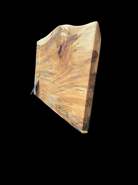 The Ambrosia Live Edge Serving Tray by B. James Design & Woodwork features rich wood grain and a natural live edge, shown with a gold ribbon accent against a black background—making it an ideal, handcrafted serving piece.